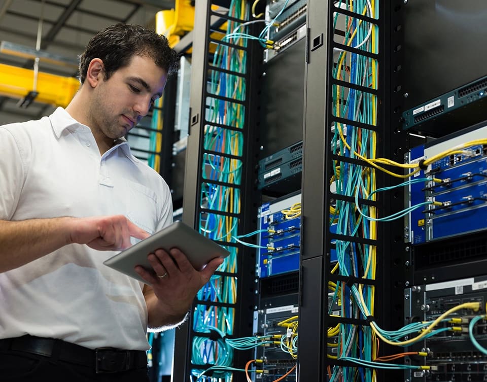 A man in white shirt holding a tablet near wires.