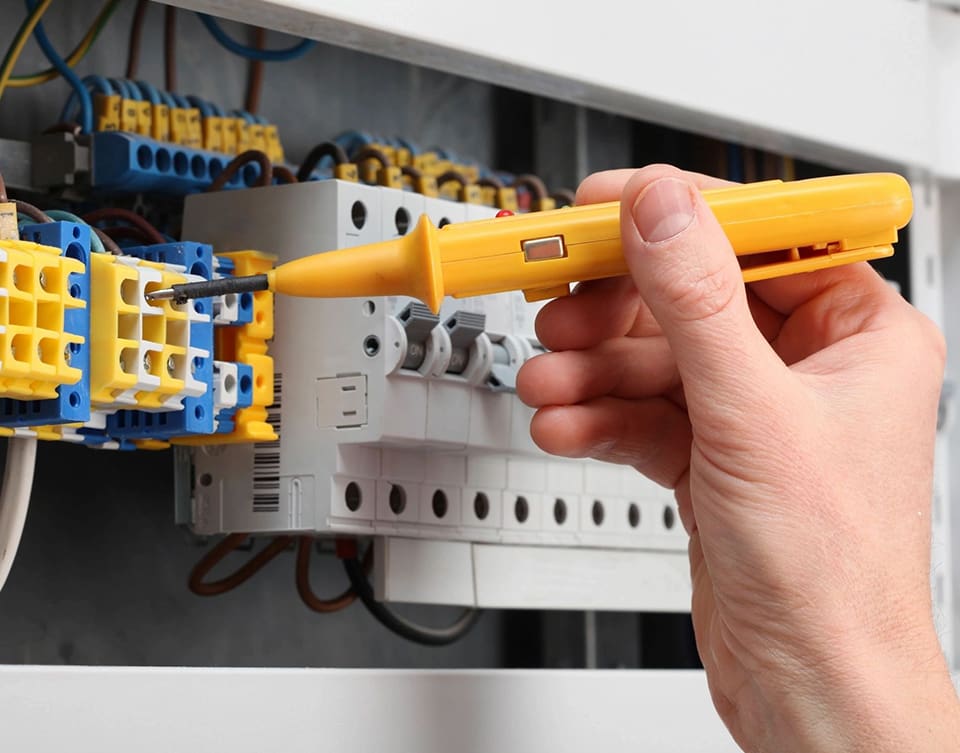 A person is holding a yellow screwdriver in front of an electrical box.