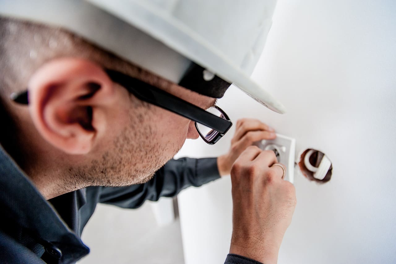 A man in glasses and hard hat fixing the wall.