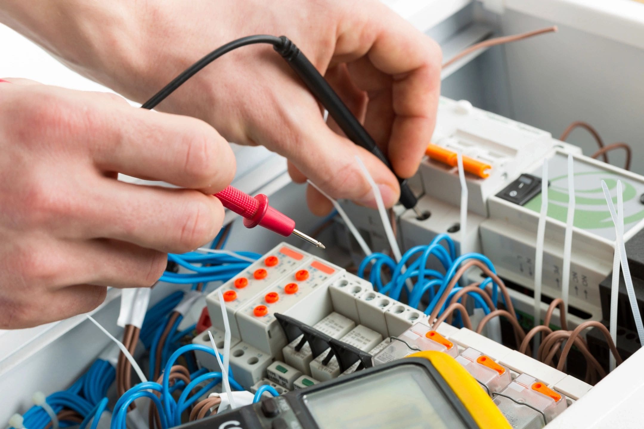 A person working on electrical equipment with wires and multimeter.